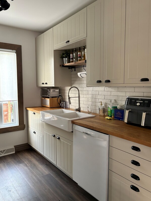 A kitchen with white cabinets, a wooden countertop, a dishwasher, and a built-in oven.