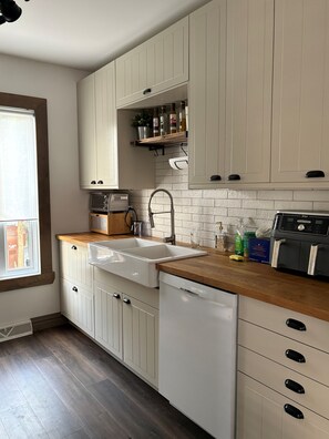 A kitchen with white cabinets, a wooden countertop, a dishwasher, and a built-in oven.