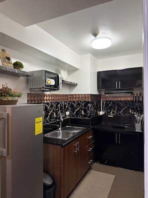 A modern kitchen with a built-in microwave, stove, and sink. There is a trash can and a refrigerator. -  1-bedroom condo with pool walking distance to NAIA Terminal 3 Pasay City (Pasay City)