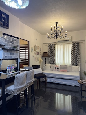 A modern living room with a sofa, a dining table with chairs, a chandelier, and patterned curtains. -  1-bedroom condo with pool walking distance to NAIA Terminal 3 Pasay City (Pasay City)