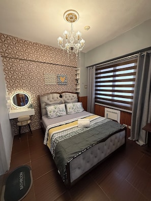 A bedroom with a tufted bed, a vanity with a mirror, a chandelier, geometric wall paneling, and a window with blinds. -  1-bedroom condo with pool walking distance to NAIA Terminal 3 Pasay City (Pasay City)