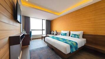 Een moderne hotelkamer met een houten hoofdbord, een groot bed, een flatscreen televisie, een bureau en een raam met gordijnen.