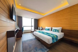 Una habitación de hotel moderna con cabecera de madera, una cama grande, un televisor de pantalla plana, un escritorio y una ventana con cortinas.