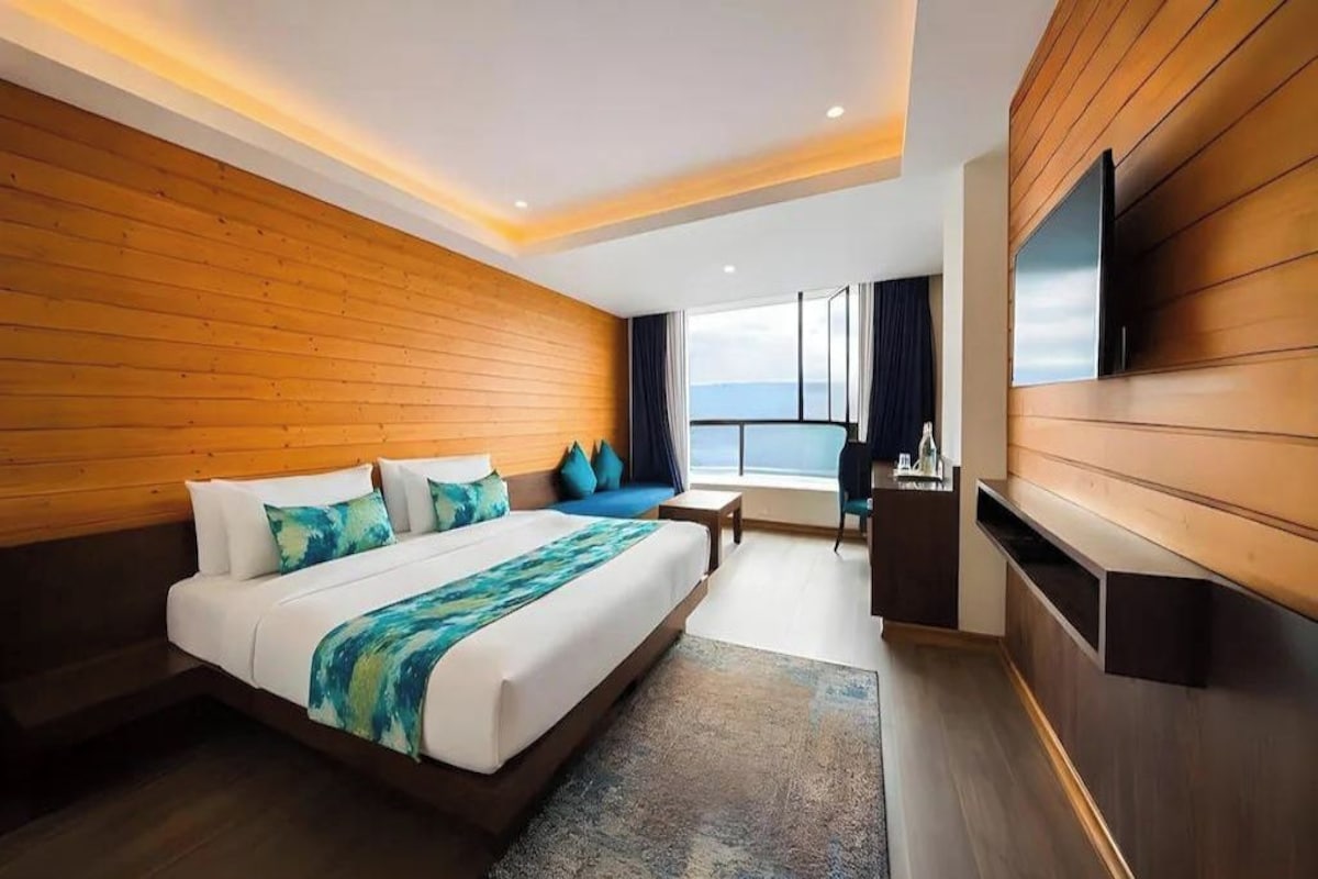 Habitación de hotel moderna con una cama grande, paneles de madera, un televisor de pantalla plana y vistas al cielo.