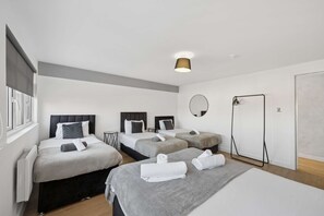 A hotel room with three beds, a round mirror, a standing lamp, and a wardrobe. - Sleek Spacious 2BR Apartment in Liverpool (Liverpool)