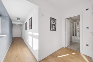 A hallway with wooden flooring, white walls, and framed pictures. There is a door leading to a bathroom with a shower. - Sleek Spacious 2BR Apartment in Liverpool (Liverpool)
