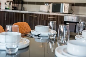 A dining table set with white plates, bowls, and glasses, with a microwave and toaster in the background. - Sleek Spacious 2BR Apartment in Liverpool (Liverpool)