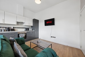 A modern kitchen with white cabinets, a coffee machine, and a flat-screen TV mounted on the wall displaying 'NETFLIX'. - Stylish 2BR Liverpool City Centre Apartment (Liverpool)