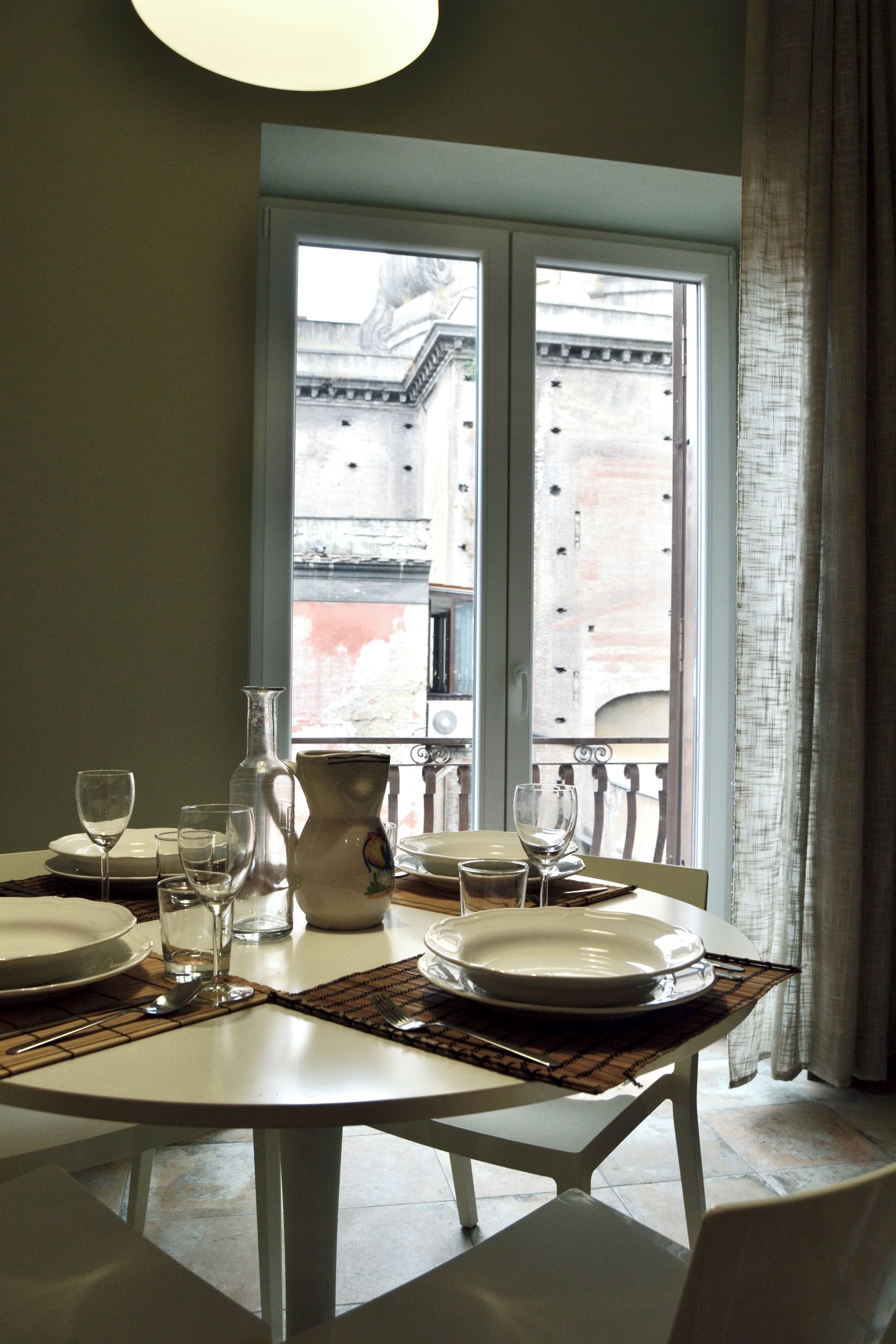 A dining table set with plates, glasses, and cutlery, with a view of a building through a window.