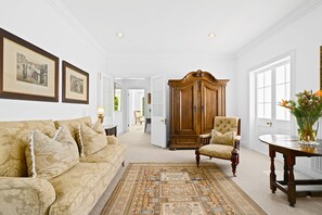 A spacious room with a large wooden armoire, a patterned sofa, and a traditional chair. - Raithbury Hill House (Stellenbosch)