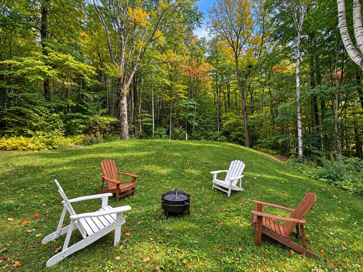 A grassy outdoor area with three Adirondack chairs and a fire pit.