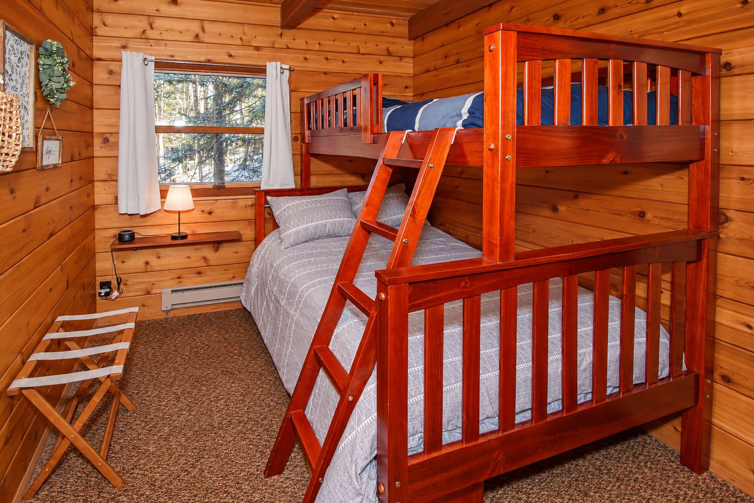 Una cama litera con escalera, una mesita de noche, una lámpara y una ventana con cortinas.