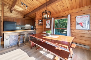 Een houten hut binnen, met een keuken, een eethoek en een groot raam.