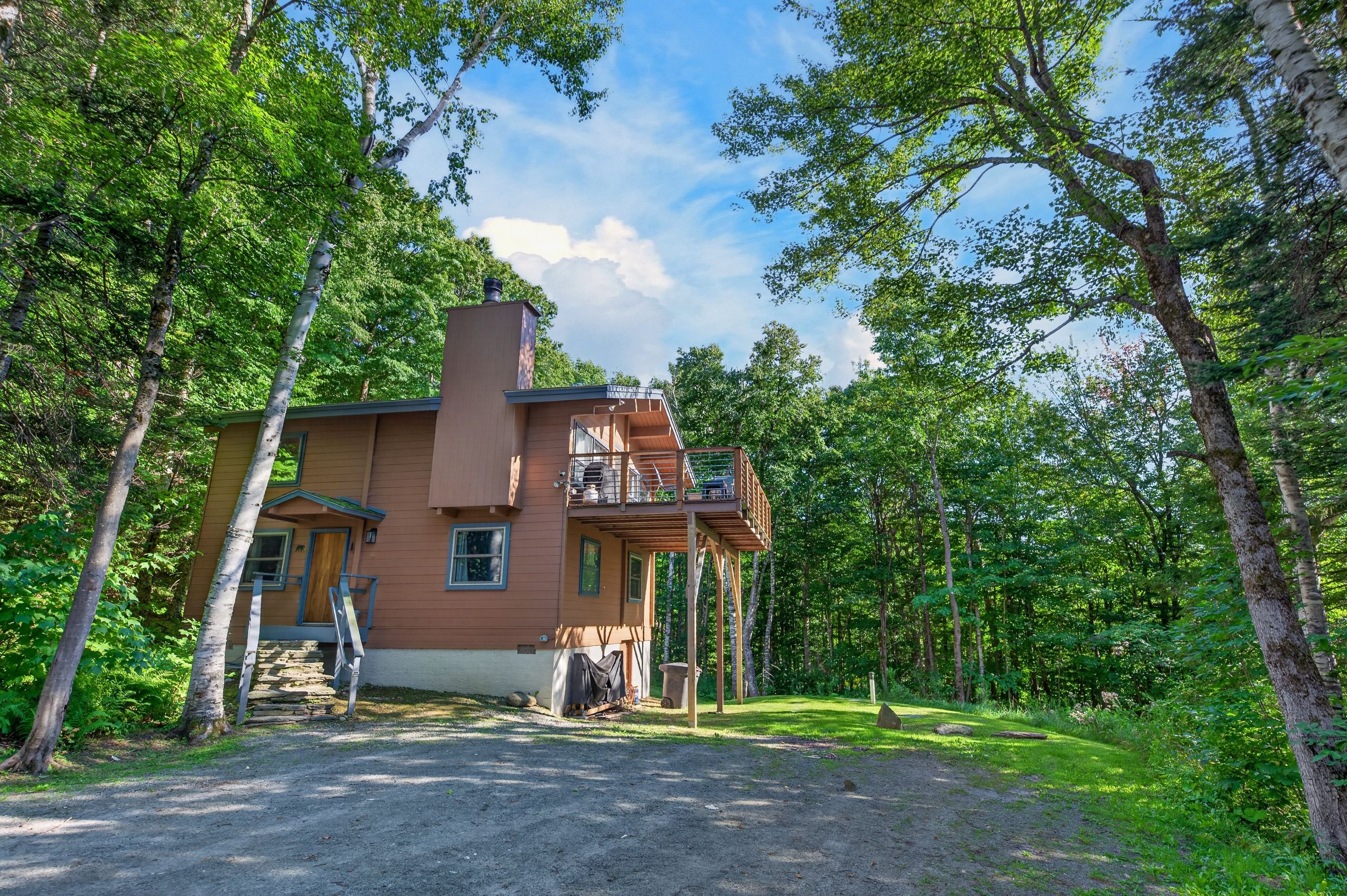 Een chalet met twee verdiepingen en een balkon, omringd door een bos.