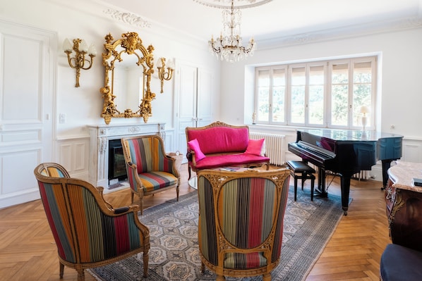 A room with a grand piano, ornate chairs, a fireplace, and a large mirror. - Le Clos du Breuchin (Breuchotte)