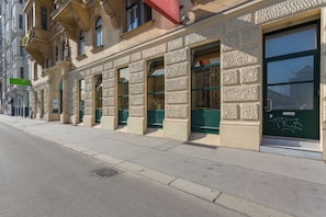 A building facade with multiple windows and doors, some with green frames, and a visible manhole cover on the sidewalk. - 1-Bedroom Apartment | Naschmarkt | 4 Guests | Self Check-in (Wien)