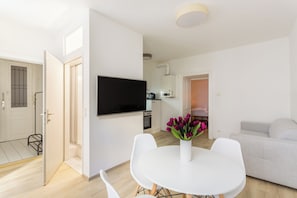 A modern living room with a flat-screen TV mounted on the wall, a dining table with chairs, and a sofa. - 1-Bedroom Apartment | Naschmarkt | 4 Guests | Self Check-in (Wien)