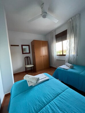 Ein Zimmer mit zwei Betten, einem Kleiderschrank, einem Sessel und einem Deckenventilator.
