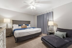 A hotel room with a bed, a nightstand, a lamp, a ceiling fan, and a window with curtains. - 4-bedroom House in Regal Oaks Near Disney (Kissimmee)