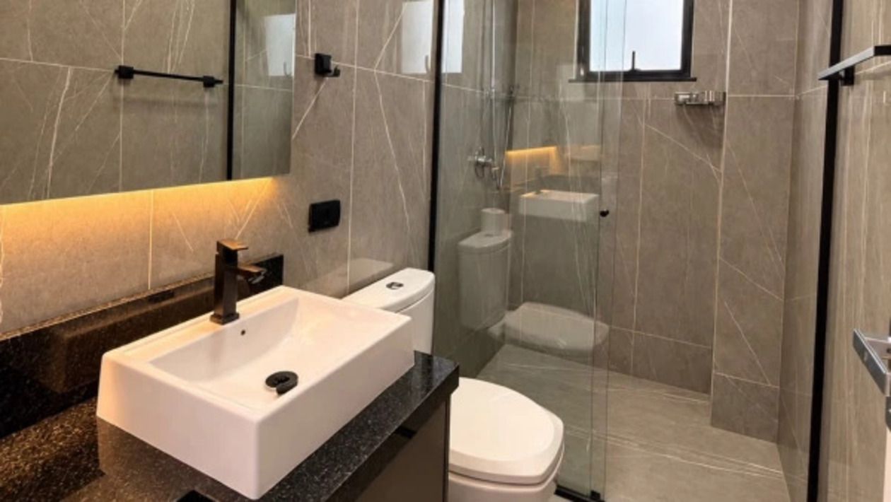 A modern bathroom with a glass-enclosed shower, a white sink, and a toilet.