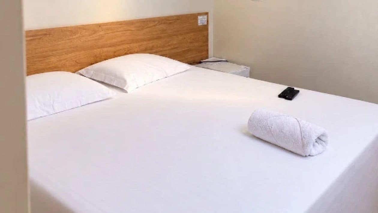 Een opgemaakt bed met witte lakens en een houten hoofdeinde.