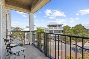 A balcony with a table and chairs, overlooking a residential area with houses and trees. - Sea Sanctuary (Panama City Beach)