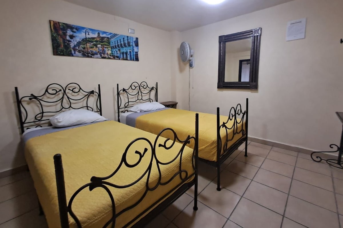 A room with two beds, a ceiling fan, a wall-mounted mirror, and a painting.