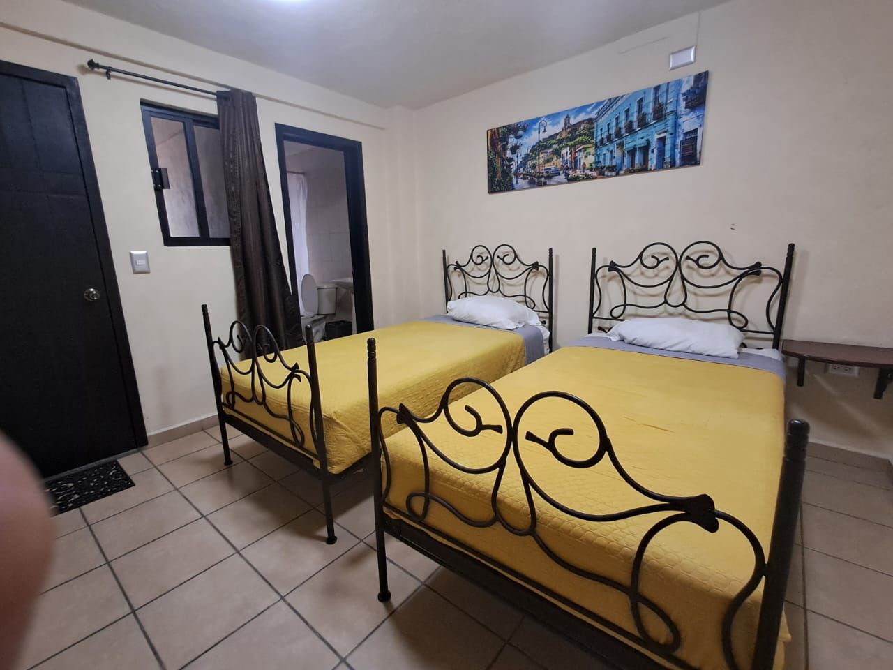 A room with two beds, a door, a window, and a painting on the wall.