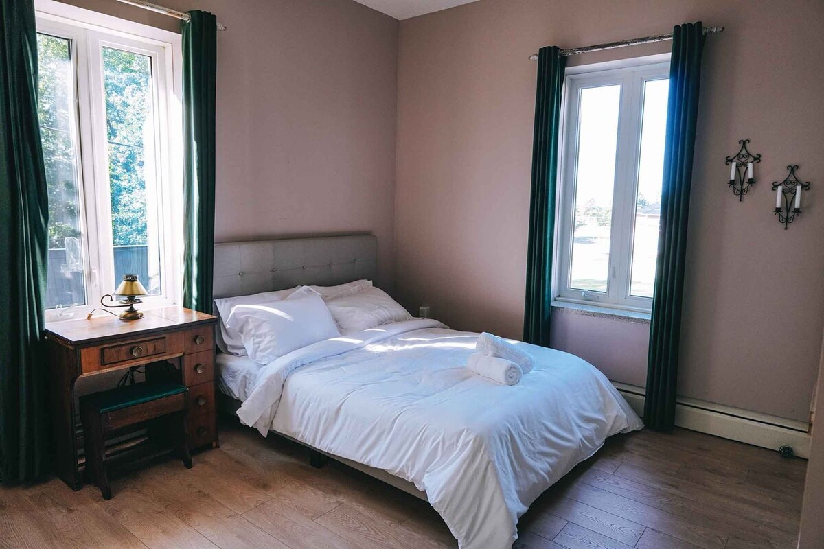 Une chambre à coucher avec un lit, un bureau et deux fenêtres avec des rideaux.