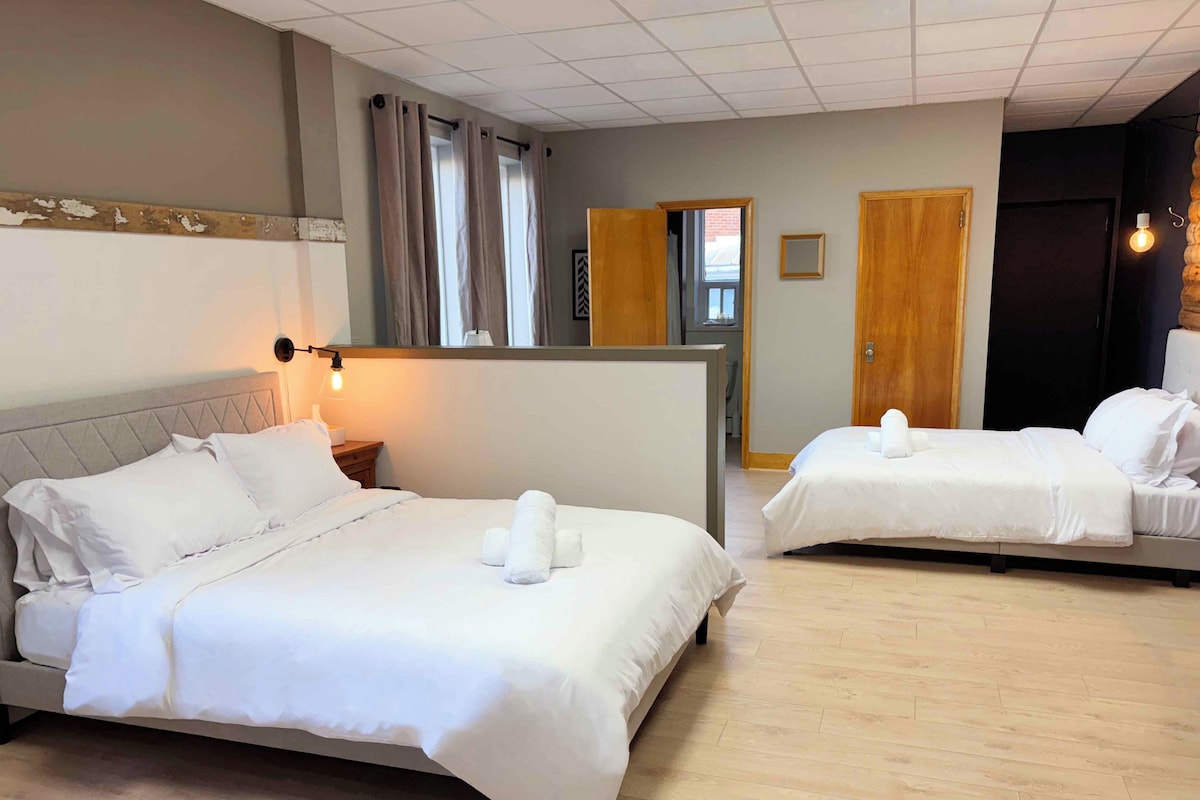 A hotel room with two beds, a wooden headboard, a nightstand, and a wall-mounted light.