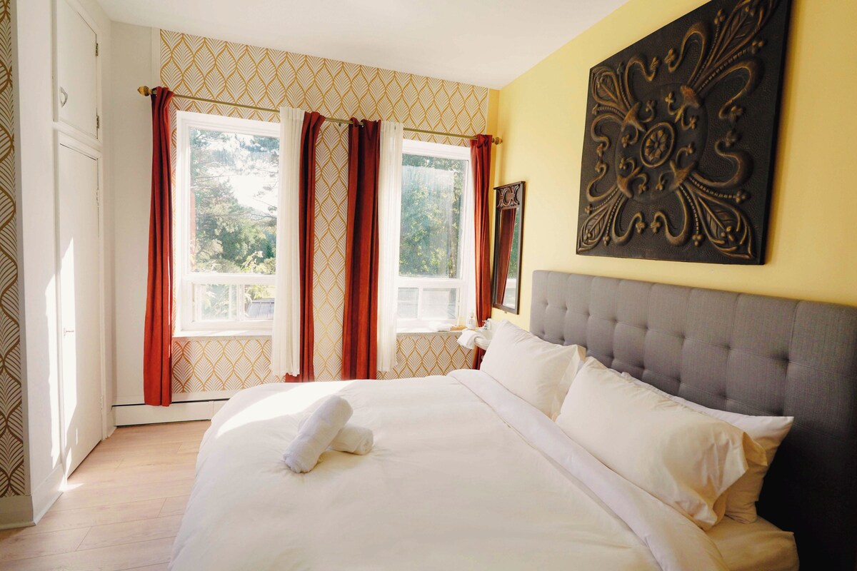 A hotel room with a large bed, a headboard, and a window with curtains.