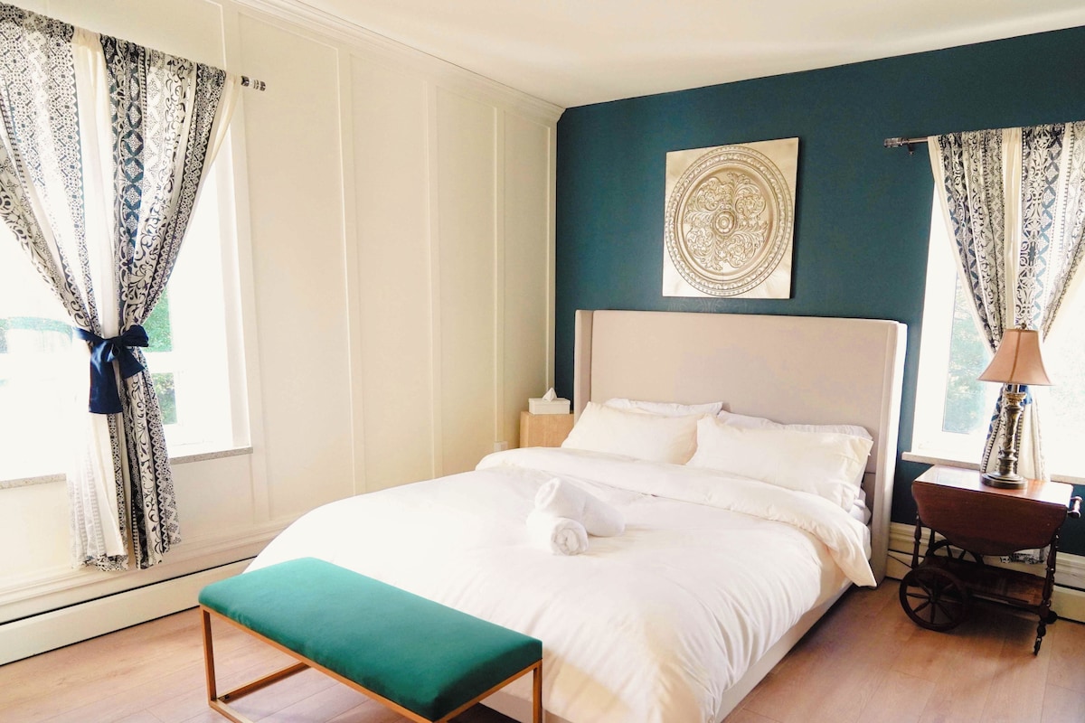 A bedroom with a bed, a bedside table, a lamp, a bench, and curtains.