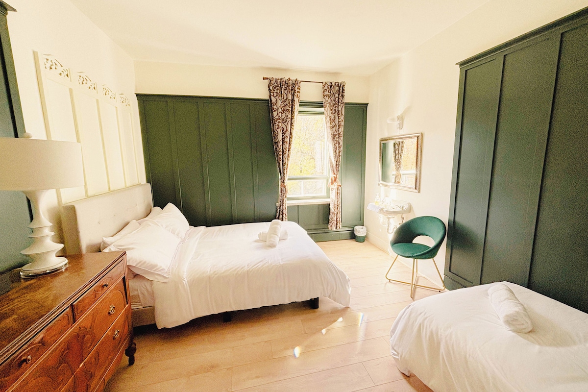 A hotel room with two beds, a dresser, a chair, a window with curtains, and a mirror.