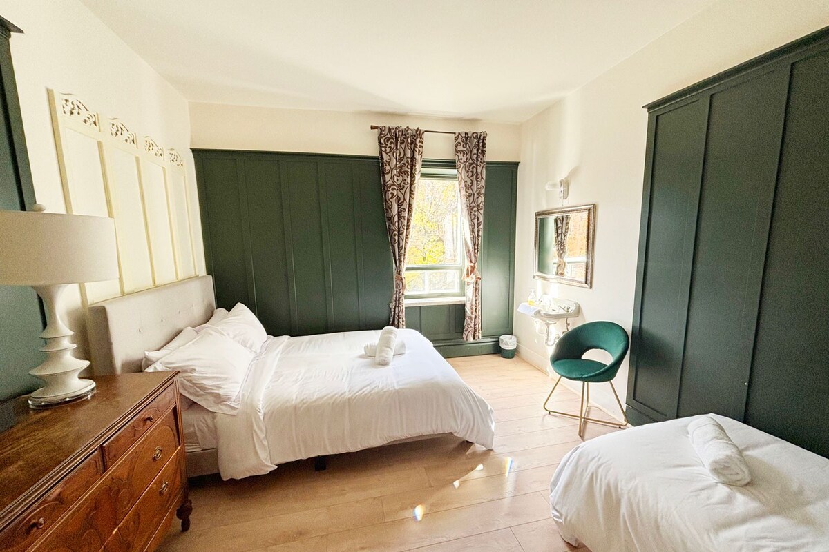 Une chambre d’hôtel avec deux lits, une commode, une coiffeuse avec un miroir et une fenêtre avec des rideaux.