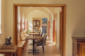A dining area with a long table and benches, an arched doorway leading to another room, and a decorative cabinet.