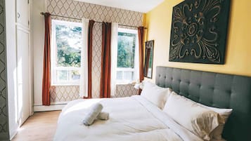 Habitación de hotel con una cama grande, cabecera, ventana con cortinas y una obra de arte colgada en la pared.