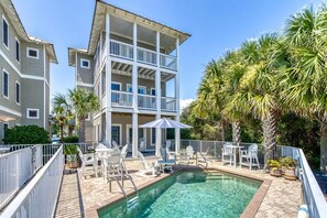 A pool area with lounge chairs and umbrellas, surrounded by a multi-story building with balconies. - Sandy Knickers (Panama City Beach)
