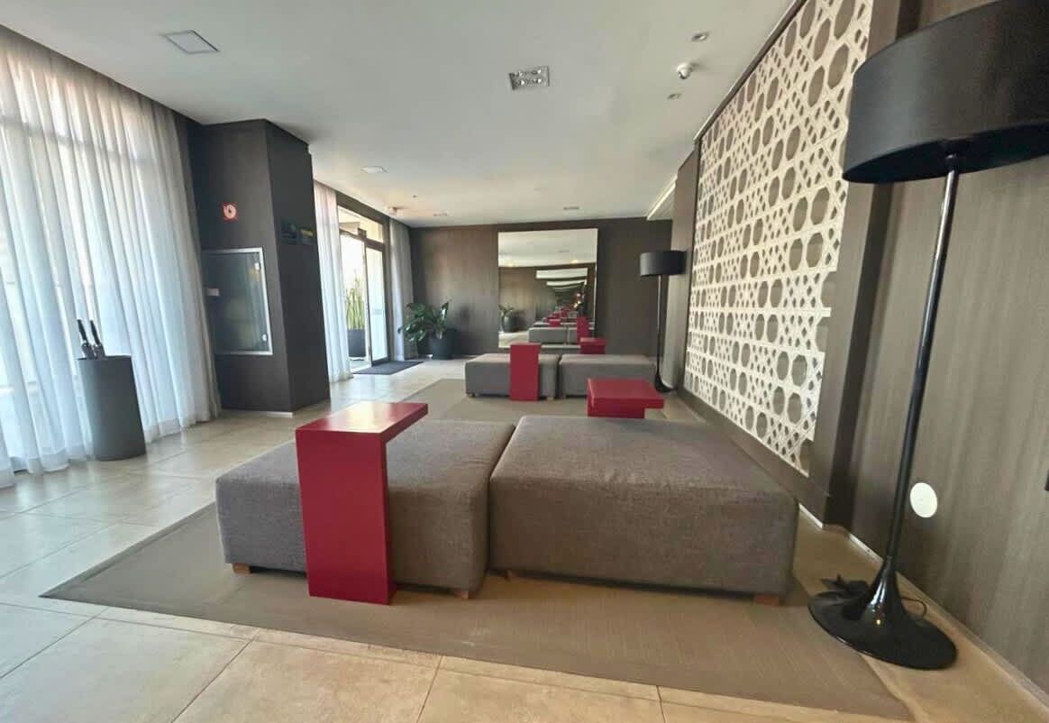 Un hall d’hôtel moderne avec un canapé d’angle, une petite table d’appoint rouge et un mur orné d’un motif.