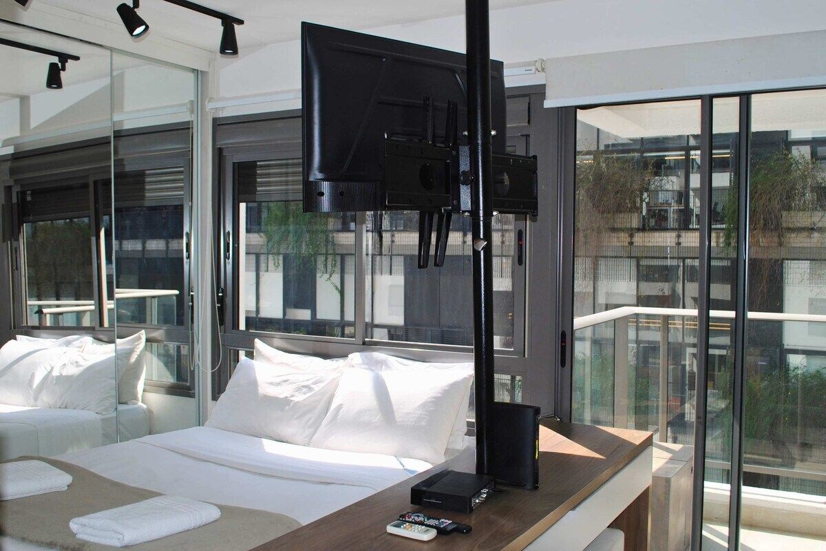 Ein modernes Hotelzimmer mit einem großen Bett, einem flachbildfernseher an der Wand, einem Nachttisch aus Holz und einem großen Fenster mit Blick auf die Stadt.