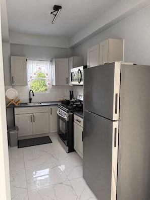A modern kitchen with white cabinets, a stainless steel refrigerator, a microwave, and a stove. - Zu Casa | Peaceful 2-Bedroom Apartment in Historic Parham, Antigua (Saint Peter’s)