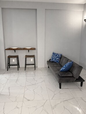 A modern living room with a grey sofa, two wooden stools, and a marble floor. - Zu Casa | Peaceful 2-Bedroom Apartment in Historic Parham, Antigua (Saint Peter’s)
