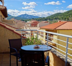 Ein Balkon mit Tisch und Stühlen, mit Blick auf eine Stadt mit roten Dächern und einem Berg in der Ferne.