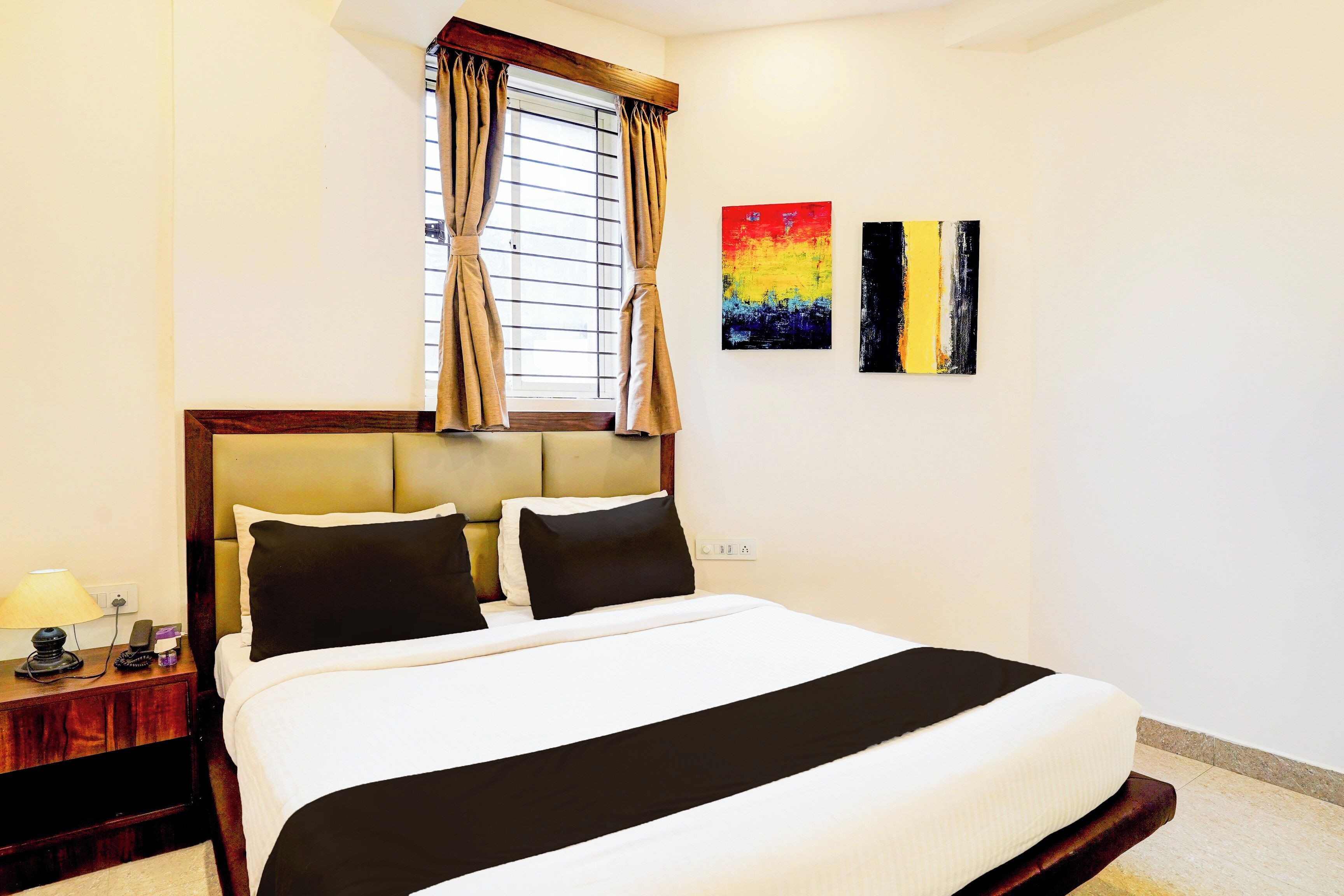 A hotel room with a bed, a nightstand, a lamp, and two paintings on the wall.