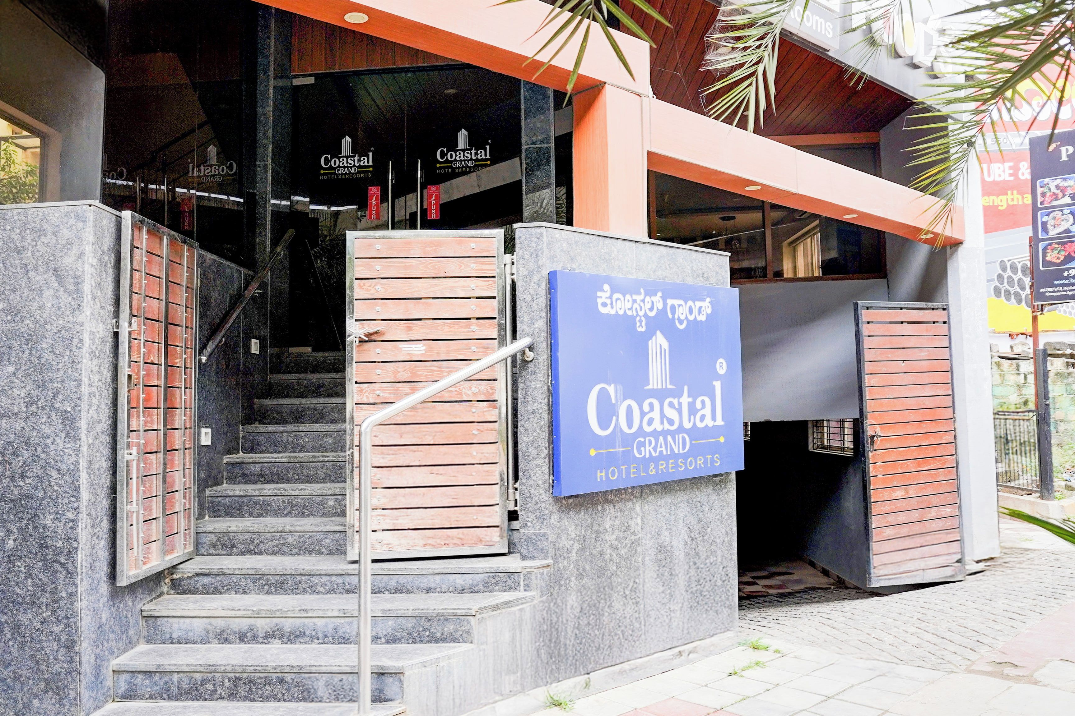 Entrada de un hotel con un cartel que dice Coastal Grand Hotel & Resorts, mostrando una escalera y un acceso con puerta de reja.