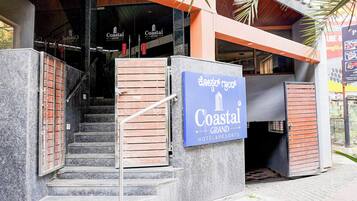 Entrada de un hotel con un cartel que dice Coastal Grand Hotel & Resorts, mostrando una escalera y un acceso con puerta de reja.