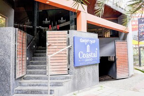 Entrada de un hotel con un cartel que dice Coastal Grand Hotel & Resorts, mostrando una escalera y un acceso con puerta de reja.