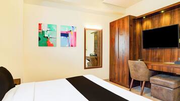 Habitación de hotel con cama, escritorio, silla, televisor de pantalla plana y dos cuadros abstractos en la pared.