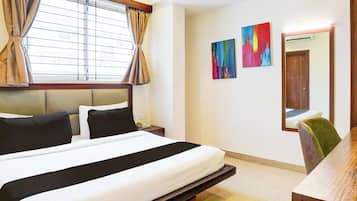 Habitación de hotel con cama, mesita de noche, teléfono, espejo y dos cuadros abstractos en la pared.