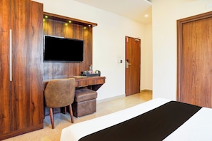 Habitación de hotel con una cama, un escritorio con silla, un televisor fijado a la pared y un armario de madera.