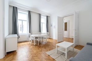 A spacious living room with a wooden herringbone floor, a white dining table with chairs, a grey sofa, and a white coffee table. - 2-Bedroom Apartment with Elevator | Naschmarkt | Sleeps 6 (Wien)
